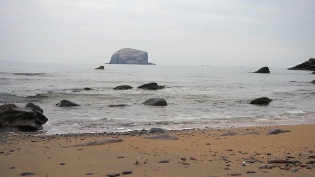  Big waves crashing against a golden sandy beach with Bass Rock producly sitting in the background. 4K VIDEO 