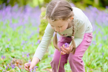 Young girl happy laughing picking bluebell flowers outside in spring summer forest woodland