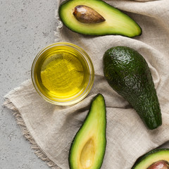 Halves and whole avocadoes and bowl of oil on napkin