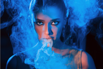 Young woman smoking vape or e-cigarette in neon light
