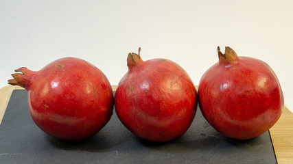 Bright juicy pomegranate fruits, white background, in the photo next three fruits are hardly placed, fruit is placed on a stone kitchen board, close-up