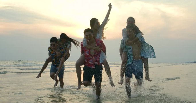 Group of friends giving piggyback rides to girls at the beach in slow motion. Summer, Travel and Beauty concept.