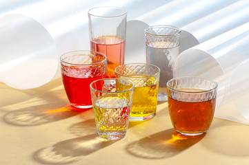 Multicolored soft drinks in glass cut glasses on a yellow table.