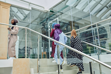 Multiracial group of muslim business women visiting international conference at business centre, walking up the staircase sharing impressions and ideas after event