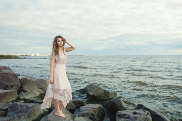 Pretty model in beige dress on ocean coast. Romantic portrait of beautiful young woman