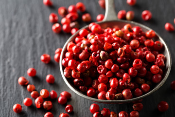 Pink or rose brazilian red peppercorns (schinus terebinthifolius) in metal spoon on black background