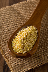 Pile of golden millet, a gluten free grain seed, in wooden spoon on burlap fabric on brown kitchen table