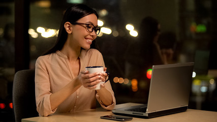 Smiling female freelancer enjoying hot tea working laptop in cafe, relaxation