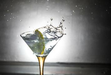 Martini cocktail glass in hand splashing on dark toned smoky background or colorful cocktail in glass with splashes and olives. Party club entertainment. Mixed light. Selective focus