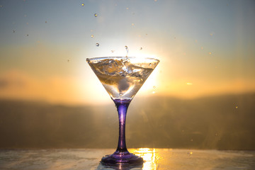 Martini cocktail glass in hand splashing on dark toned smoky background or colorful cocktail in glass with splashes and olives. Party club entertainment. Mixed light. Selective focus