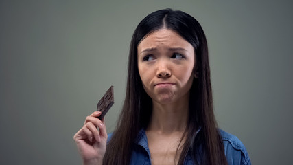 Fototapeta premium Sad asian girl dreaming about sweet chocolate keeping diet, healthy nutrition