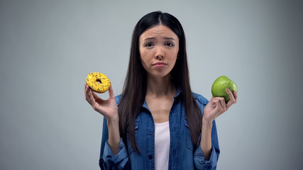 Hungry girl trying to choose between donut and apple, healthy eating, temptation