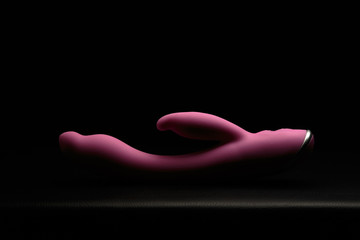 Pink dildo on black skin. Dark background. Artistic lighting.