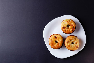 Three homemade cupcakes lying on white plate on black background. Top view with copyspace