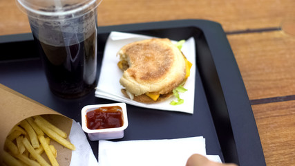 Bitten hamburger with carbonated water and fries on tray, fast food restaurant