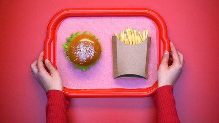 Woman putting cafe tray with french fries and burger, unhealthy snack, top view