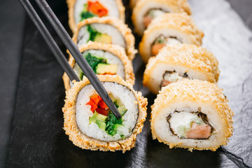 eating sushi. Chopsticks taking maki roll from plate. Japanese food, deluxe restaurant menu, delicious traditional seafood. philadelphia and vegetarian tempura rolls set