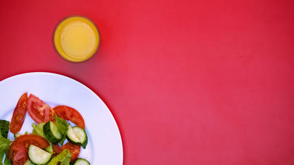 Glass with orange juice and white plate with fresh salad on bright background