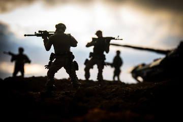 Fototapeta premium War Concept. Military silhouettes fighting scene on war fog sky background, World War Soldiers Silhouettes Below Cloudy Skyline at sunset. Attack scene. Armored vehicles.