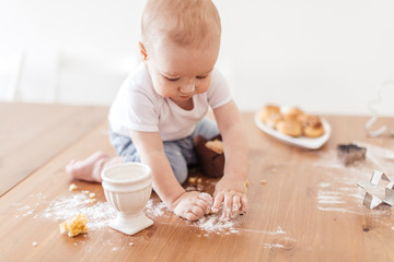 Adorable little helper cooking in kitchen. Cute little toddler crawling alone on kitchen table, covered with flour after making cakes.