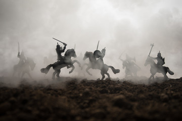 Medieval battle scene with cavalry and infantry. Silhouettes of figures as separate objects, fight between warriors on sunset foggy background. Selective focus - obrazy, fototapety, plakaty