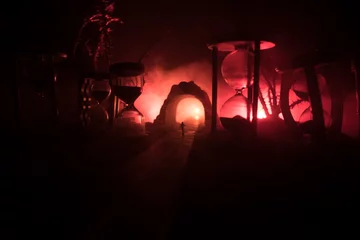 Zeitkonzept. Silhouette eines Mannes, der zwischen Sanduhren mit Rauch und Lichtern auf dunklem Hintergrund steht. Surreal dekoriertes Bild © zef art