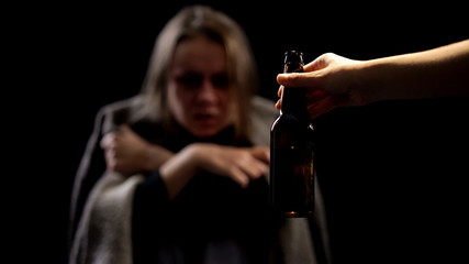 Hand offering beer bottle to alcoholic woman, miserable life, addiction concept