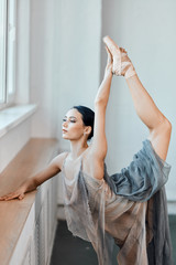 Attractive dark-haired ballet dancer female in stage costume bending back, standing on one leg doing stretching, lifting the leg up high. © alfa27