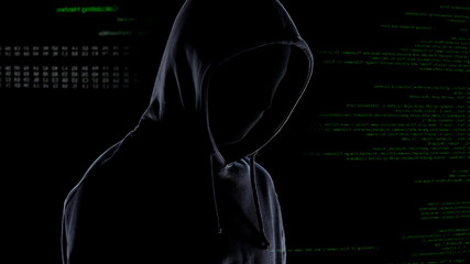 Hacker in mask and hoodie on computer code background, planning cybercrime
