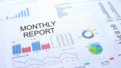 Monthly report lying on table, graphs charts and diagrams, official document