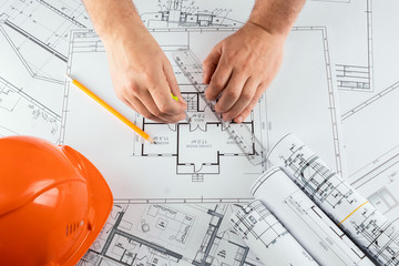 Male hands, Orange helmet, pencil, architectural construction drawings, tape measure. The architect...