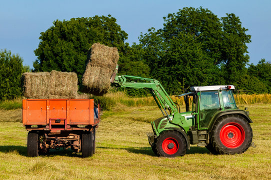 Green Tractor Loading Hay Bales On A Trailer