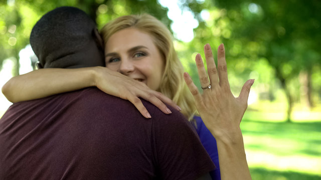 Cheerful woman embracing future husband and showing engagement ring, couple