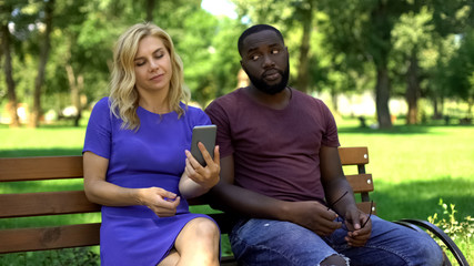 Caucasian woman playing smartphone on date in park, ignoring worried boyfriend