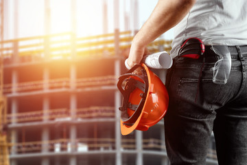 A builder, an architect holds in his hand a construction helmet against the background of a construction site, a tape measure. Concept architecture, construction, engineering, design, repair.