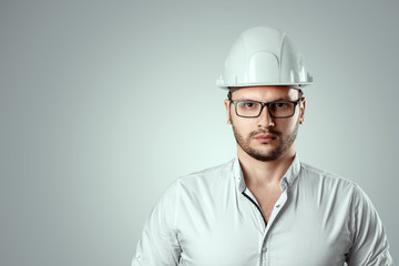 Portrait of a man in a construction white helmet on a light background. Concept architecture, construction, engineering, design, repair. Copy space