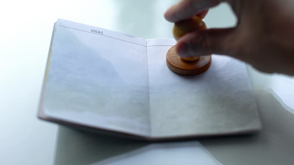 Customs officer hand stamping wooden seal in passport, travelling abroad, visa