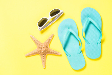 Blue flip flops, sunglasses and starfish on yellow background.