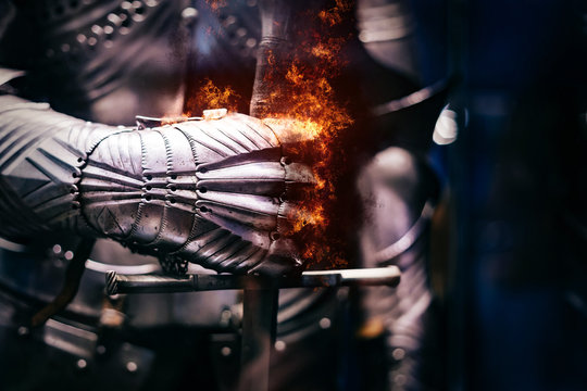 Close up of a Medieval steel armour with iron glove hand bursting with flames of fire, holding a giant sword