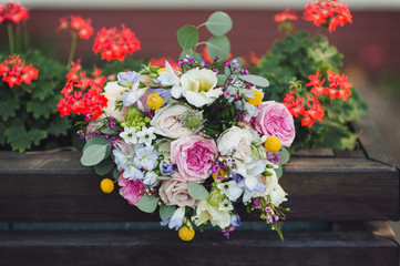 Wedding bouquet of roses and wild flowers close-up lies on a wooden chair, against the background of flowers in the garden. Wedding decorations and details.