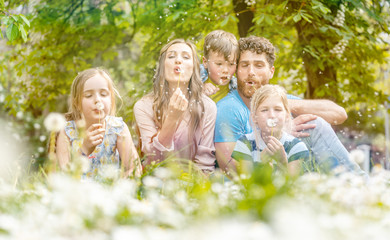 Family of five sitting on a meadow blowing dandelion flowers