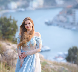 A girl with long hair on the beach. She's wearing a beautiful blue dress .    In the background...