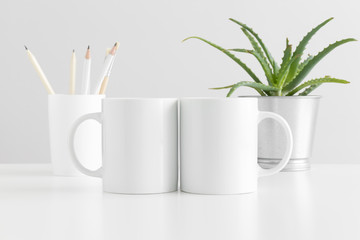 Two mugs mockup with workspace accessories and a succulent plant on a white table.
