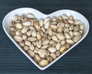 Nuts arranged in heart  on background. Healthy Food image close up pistachios on the cup plate. Love Texture on top view mock up