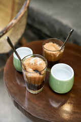 Refreshing iced coffee drinks and cups with water on round table outdoors