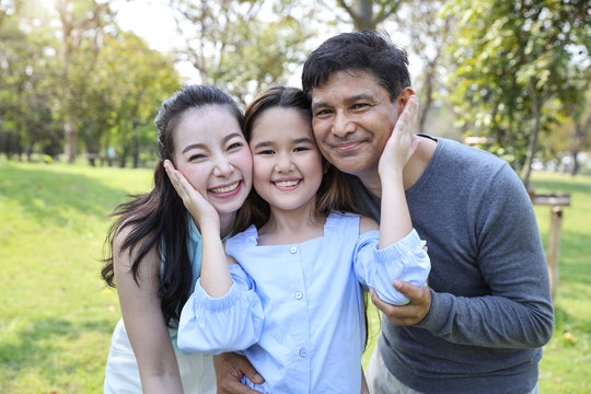 image of happy family, daughter putting her hands on parents cheek with smiling during summer time in the park