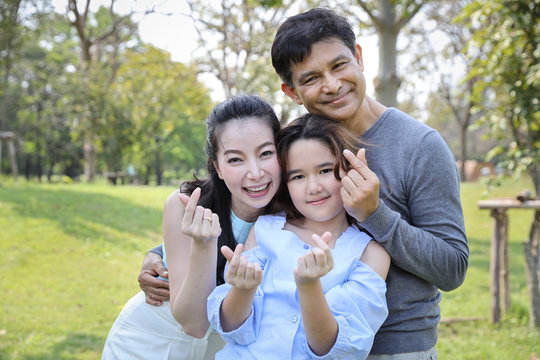 image of happy asian family, daughter and parent doing heart symbol on thier hands with smiling face during summer time in the park
