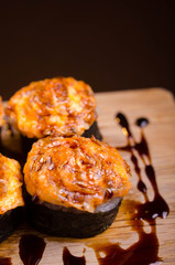 Japanese maki rolls baked with cheese and sprinkled with sauce. Sushi on a wooden plank. Seafood menu on black background