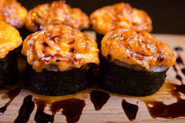 Japanese maki rolls baked with cheese and sprinkled with sauce. Sushi on a wooden plank. Seafood menu on black background
