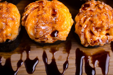 Japanese maki rolls baked with cheese and sprinkled with sauce. Sushi on a wooden plank. Seafood menu on black background